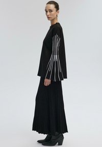 Black long-sleeve top with white vertical lines on sleeves, paired with a black pleated maxi skirt and ankle heeled boots. Smooth texture.