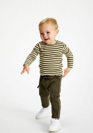 Randig långärmad skjorta i grön och beige, i kombination med olivfärgade byxor med fågelmönster, fulländad med vita sneakers.