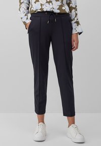 Marineblauwe broek met enkel lengte, met een trekkoord in de taille, plooidetails en zijzakken, gecombineerd met witte sneakers. Glad stoffen textuur.