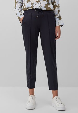 Marineblauwe broek met enkel lengte, met een trekkoord in de taille, plooidetails en zijzakken, gecombineerd met witte sneakers. Glad stoffen textuur.