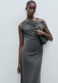 Gray sleeveless dress with a draped design, featuring a side slit and soft texture, paired with a matching green shoulder bag.