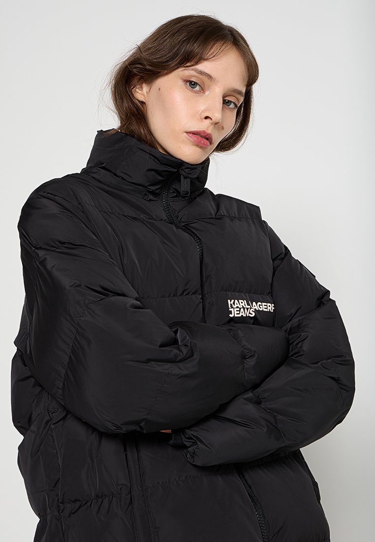 Doudoune noire avec col montant, fermeture éclair à l'avant et logo brodé sur la poitrine. Présente un design matelassé et une silhouette oversize.
