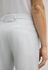 Pantalons gris texturé avec une coupe slim, poches arrière et passants de ceinture, avec une surface en tissu doux et un design ajusté.