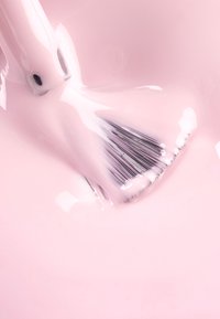 Pennello da trucco con setole nere parzialmente immerso in una sostanza rosa lucida, che mostra una superficie liscia e riflettente e curve morbide.