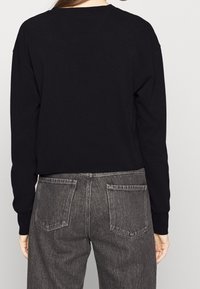 Maglia nera a maniche lunghe con spalle scese, abbinata a jeans di denim grigi a vita alta con due tasche posteriori e una texture scolorita.