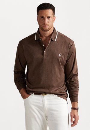 Bruine polo met lange mouwen en een witte kraag, voorzien van een klein logo op de borst. Draag het met een witte broek, wat een ontspannen pasvorm laat zien.