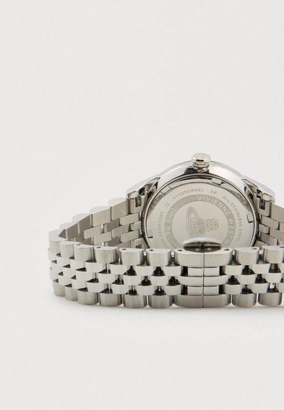 Sudraba krāsas nerūsējošā tērauda Vivienne Westwood rokas pulksteņa aizmugure ar saistītu siksniņu un iegravētu logotipu uz korpusa aizmugures.