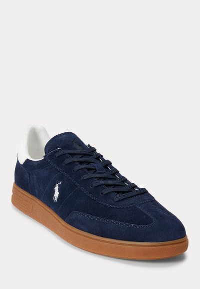 Tamsiai mėlyni zomšiniai sportbačiai su gumine pado danga, balta kulno papildoma dalimi, tamsiai mėlynomis raišteliais ir baltu Polo Ralph Lauren logotipu šone ir liežuvėlyje.