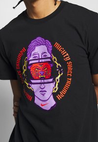 Musta lyhythihainen t-paita, jossa on elävä grafiikkasuunnitelma kahdesta tyylitellystä päästä, joissa on tiikeri ja ketjuja, käyttäen purppuraa, punaista ja oranssia väriä.