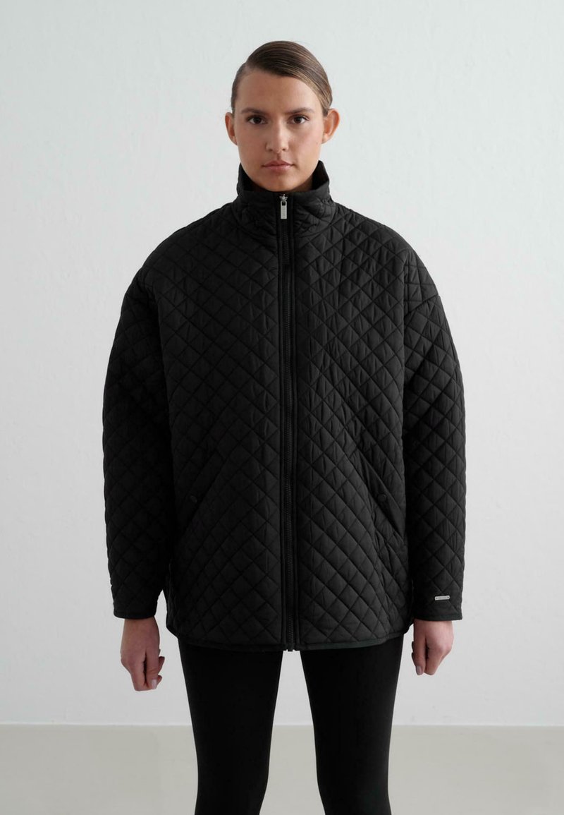 Chaqueta negra acolchada con cuello alto, cremallera frontal y bolsillos laterales. Presenta un diseño estructurado y oversize con un patrón de diamante texturizado.