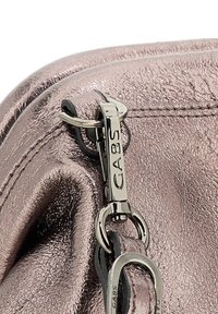 Angolo di una borsa in pelle metallica rosa, che mette in mostra una superficie strutturata e hardware della cerniera di tonalità argentata con un'etichetta incisa "GABS" e un anello.