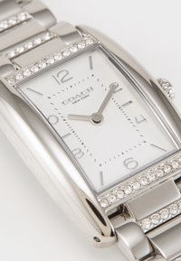 Silver stainless steel watch with rectangular case, white dial, black numerals, and crystal accents on bezel and bracelet links.