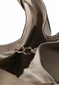 Beżowa skórzana torba typu tote o gładkiej fakturze, zewnętrzną kieszenią, złotymi akcentami oraz zapięciem na zamek. Posiada mocny, szeroki pasek.