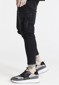 Svarta cargobyxor med sidfickor och spänndetalj, tillsammans med svarta och grå sneakers som har mesh- och mockamaterial.