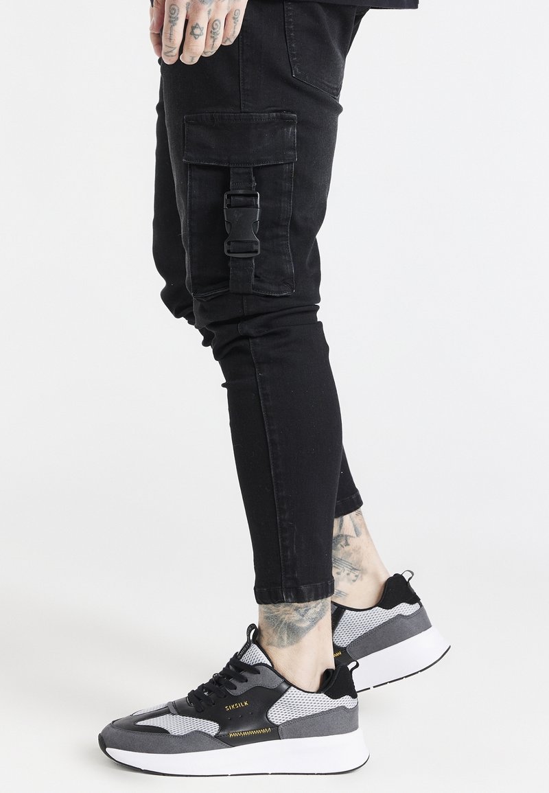 Svarta cargobyxor med sidfickor och spänndetalj, tillsammans med svarta och grå sneakers som har mesh- och mockamaterial.