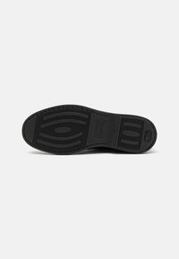 Suela de zapato de goma negra con un patrón de banda de rodadura intrincado, forma plana y textura suave con detalle de marca incrustado.