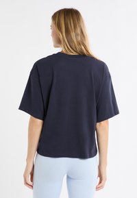 T-shirt en coton bleu marine avec une coupe décontractée, manches courtes, encolure ronde et ourlet raccourci. Texture lisse sans motifs visibles.