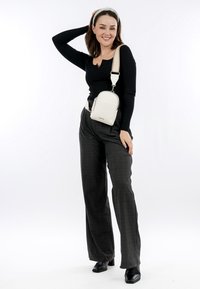 Bílá strukturovaná crossbody taška se zipovým uzávěrem, nastavitelným popruhem a minimalistickým designem. Model má na sobě černý top a šedé kostkované kalhoty.