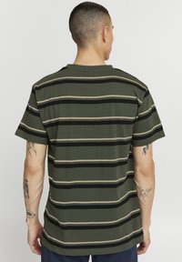 Camiseta de rayas verdes con rayas horizontales negras y beige, de mangas cortas y un corte relajado. Espalda lisa sin logotipos ni diseños visibles.