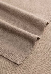 Soft beige knitted fabric with a ribbed edge, folded to show texture and thickness.