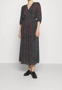 Mörkgrön klänning med blommönster i rött och rosa. V-ringning, trekvartsärmar, åtsittande midja, flödande kjol, i kombination med svarta loafers.