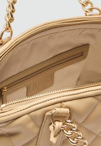 Beige, gequilted handtas met hardware in goudkleur, met een binnenzak, ritssluiting en leren merktekens. Glad textuur aan de binnenkant.