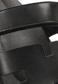 Sandalias de cuero negro con tiras anchas con formas recortadas, una textura suave y un diseño minimalista, adecuadas para el uso casual.