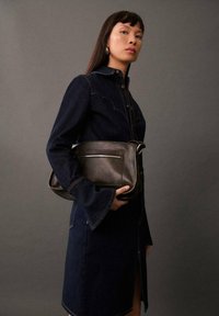 Denim obleka z dolgimi rokavi in gumbi spredaj, ujemajoča se z rjavim usnjenim nahrbtnikom s poštnim žepom.