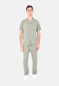 Camicia verde chiaro a maniche corte con taschino frontale, abbinata a pantaloni tapered coordinati. Il tessuto appare liscio; abbinata a sneakers bianche.