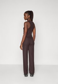 Sorte, ribbede jumpsuit med et tætsiddende top og vidde ben, der har en rygdesign med detaljer og en glat tekstur.