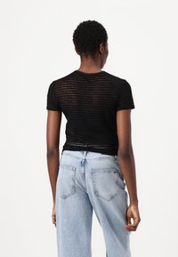 Svart, tettsittende t-skjorte med teksturert mønster, korte ermer og rund hals, sammen med lyseblå høytlivsjeans.