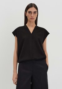 Schwarzes, geripptes Oberteil mit V-Ausschnitt und kurzen Ärmeln, kombiniert mit dunklen Hosen. Hat eine lockere Passform und weiche Textur. Einfaches Design.