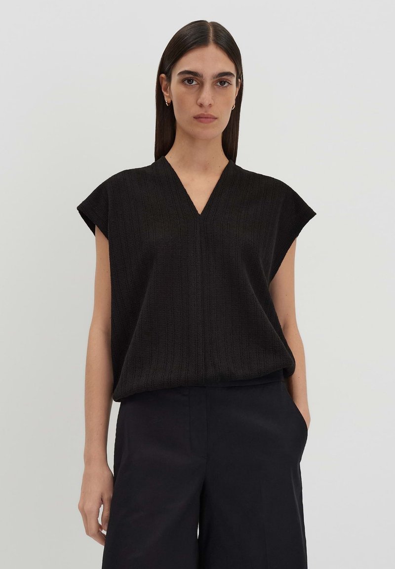 Schwarzes, geripptes Oberteil mit V-Ausschnitt und kurzen Ärmeln, kombiniert mit dunklen Hosen. Hat eine lockere Passform und weiche Textur. Einfaches Design.