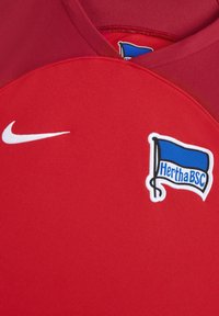 Maglia atletica rossa realizzata in tessuto testurizzato, con logo Nike bianco e uno stemma del club ricamato con una bandiera blu e "HerthaBSC."
