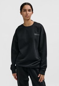 Svart överdimensionerad sweatshirt med rund halsringning och långa ärmar. Har vit text "HALO 19861972" på framsidan. Mjuk bomullsmaterial.