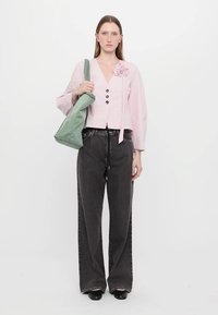 Blusa a righe rosa con dettaglio floreale, pantaloni neri a gamba larga e borsa a tracolla verde. La modella è in piedi davanti a uno sfondo bianco.