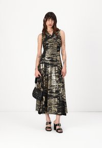 Rochie din paiete negre și aurii cu un corset ajustat, fustă evazată și design fără mâneci, asortată cu o geantă din piele ecologică neagră și sandale masive.