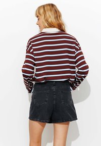 Chemise à manches longues rayée marron et bleue associée à un short en denim noir. La chemise a un col classique et une coupe légèrement oversize.