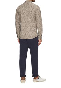 Lange mouwen blouse in beige met een subtiel stippenpatroon, gecombineerd met marineblauwe broek. Schoeisel is wit en grijs, met opgerolde cuffs op de broek.