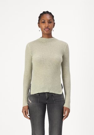 Ribbed long-sleeve sweater in light green, featuring a high neckline and a slightly cropped hem. Worn with dark grey jeans.