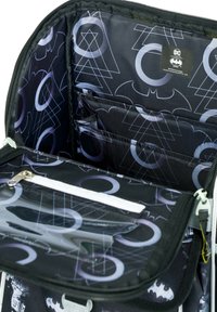 Interno di una borsa nera con finitura lucida, caratterizzato da un motivo con il logo di Batman in grigio, tasca con zip e diversi scomparti per l'organizzazione.