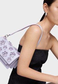 Lavender handbag with floral embellishments and a smooth texture, featuring a shoulder strap and metallic hardware.
