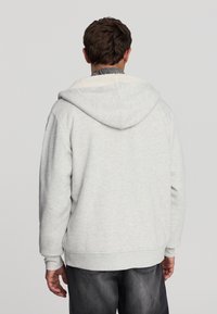 Felpa con cappuccio grigio chiaro in pile, con un morbido rivestimento interno testurizzato, dotata di un cappuccio ampio e polsini a costine. Vestibilità standard e design rilassato.