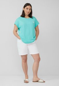 Turquoise t-shirt met korte mouwen en een ronde halslijn, gecombineerd met witte denim shorts en lichte sandalen. Eenvoudig ontwerp, casual pasvorm.