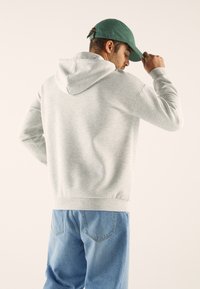 Harmaa huppari, jossa on kenguru-tasku ja säädettävä nyöripäällinen, yhdistettynä vaaleansinisiin farkk jeansseihin. Kangas näyttää pehmeältä ja teksturoidulta.