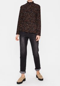 Blusa nera a maniche lunghe con motivo a macchie multicolori; presenta un colletto alto arricciato. Abbinata a jeans scuri e mocassini beige.