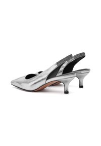 Tacones de pala plateados con puntera afilada, que presentan cortes y una parte trasera texturizada. Tacones bajos y delgados con un acento negro en la base.