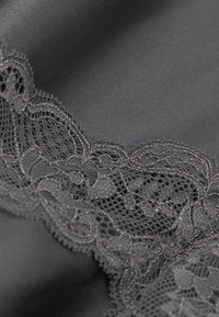 El tejido de satén negro presenta un intrincado borde de encaje gris oscuro, que muestra un delicado patrón floral y un diseño en forma de concha.