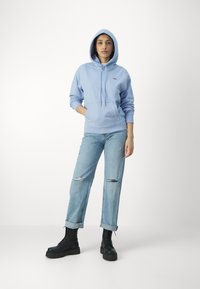 Felpa azzurra con tasca frontale e cordini regolabili, abbinata a jeans azzurri strappati e stivaletti con tacco neri allacciati.