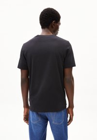 T-shirt nera in cotone con collo rotondo e maniche corte, mostrata da dietro, abbinata a un paio di jeans blu in denim.
